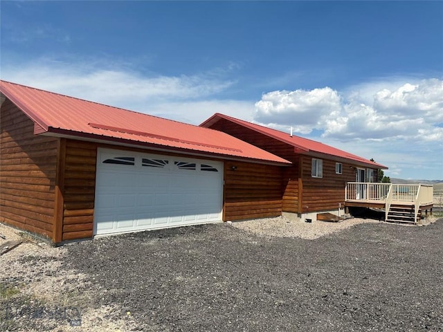 view of front facade featuring log veneer siding, metal roof, driveway, a deck, and an attached garage