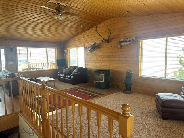 carpeted living area with a wood stove, wooden ceiling, ceiling fan, wood walls, and lofted ceiling