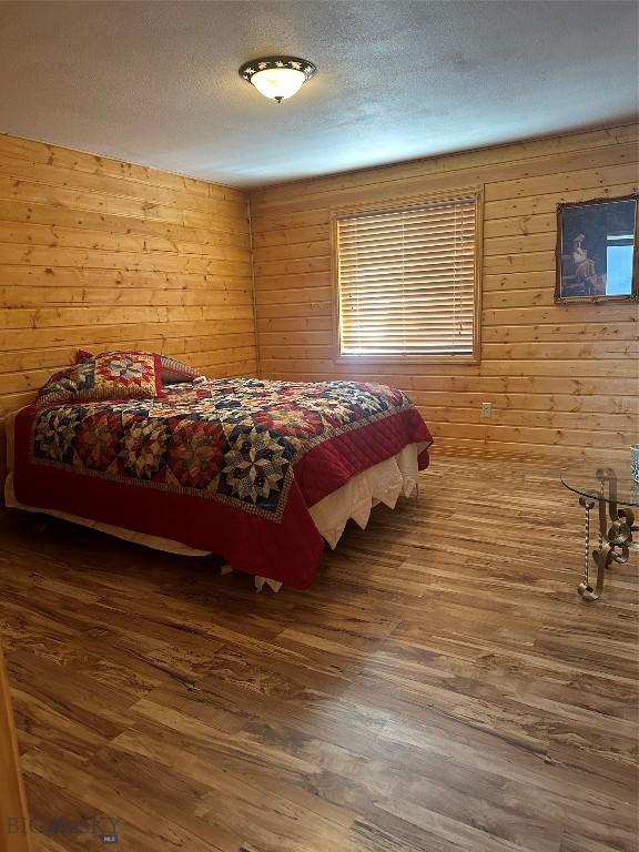 bedroom featuring a textured ceiling, wood walls, and wood finished floors