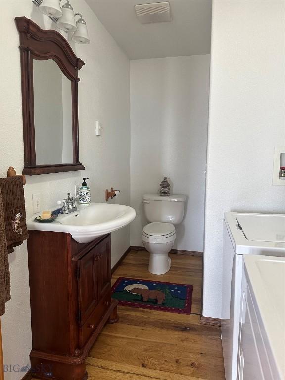 half bath featuring visible vents, baseboards, toilet, wood finished floors, and vanity
