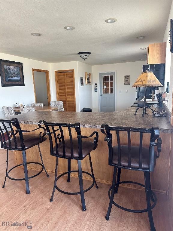interior space featuring light wood finished floors, a textured ceiling, dark countertops, and a breakfast bar