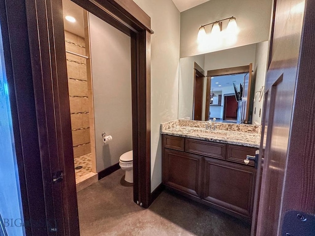 bathroom with toilet, finished concrete flooring, tiled shower, and vanity