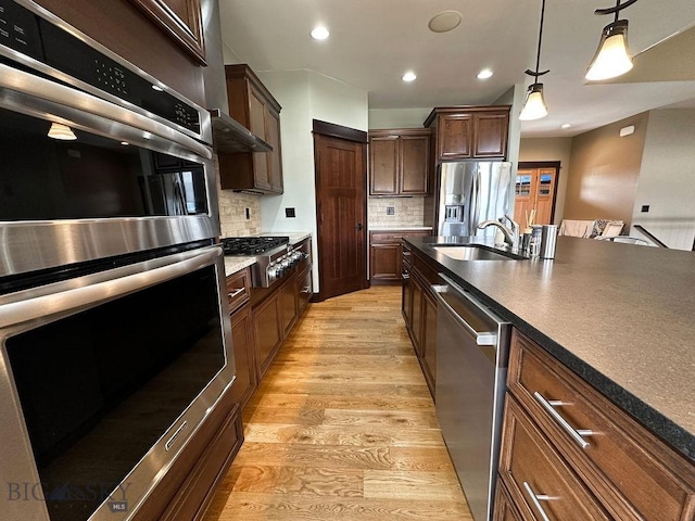 kitchen featuring a sink, stainless steel appliances, light wood-style floors, tasteful backsplash, and pendant lighting
