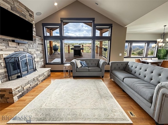living room with a notable chandelier, a stone fireplace, high vaulted ceiling, and wood finished floors