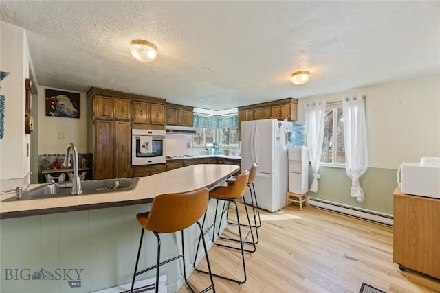 kitchen featuring plenty of natural light, a sink, a baseboard heating unit, a peninsula, and white appliances