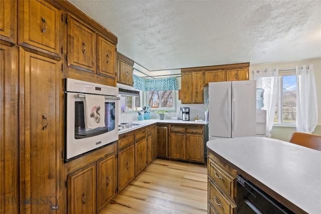 kitchen with light wood-style floors, plenty of natural light, white appliances, and a textured ceiling