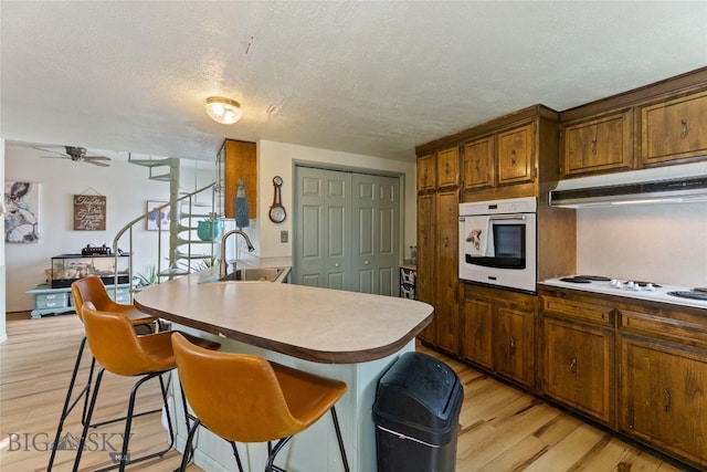 kitchen with a sink, light wood-style floors, a breakfast bar, under cabinet range hood, and white appliances