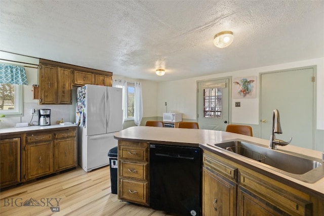 kitchen with white appliances, a textured ceiling, a sink, and light wood-style floors