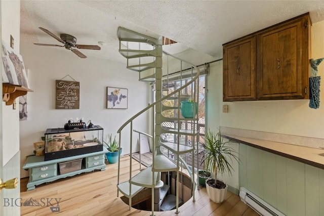staircase with a baseboard radiator, a textured ceiling, a ceiling fan, and wood finished floors