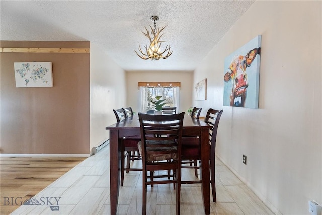 dining area featuring an inviting chandelier, a baseboard radiator, a textured ceiling, and baseboards