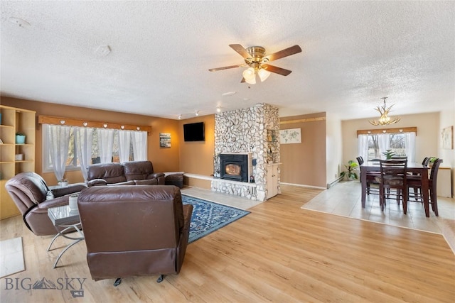 living area featuring a stone fireplace, a ceiling fan, light wood-type flooring, and a textured ceiling