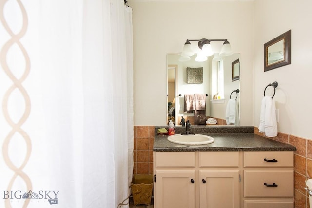 ensuite bathroom with connected bathroom, tile walls, wainscoting, and vanity