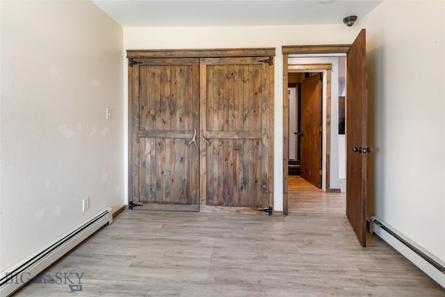 unfurnished bedroom featuring light wood-style floors, baseboard heating, and a baseboard radiator