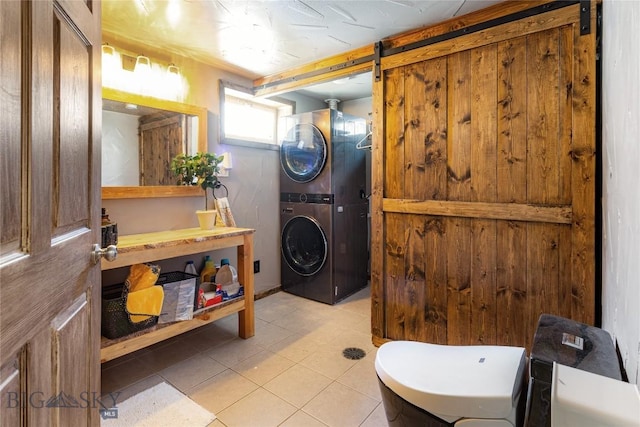 laundry area featuring stacked washing maching and dryer, tile patterned floors, laundry area, and a barn door