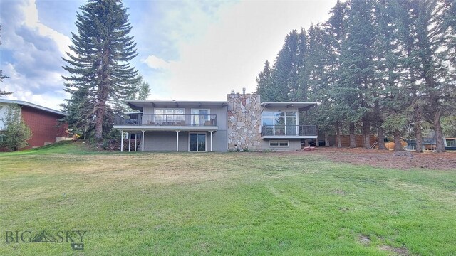 rear view of house featuring a balcony and a yard