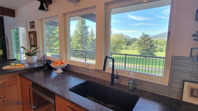 kitchen featuring brown cabinets, a sink, dark stone countertops, a mountain view, and dishwashing machine