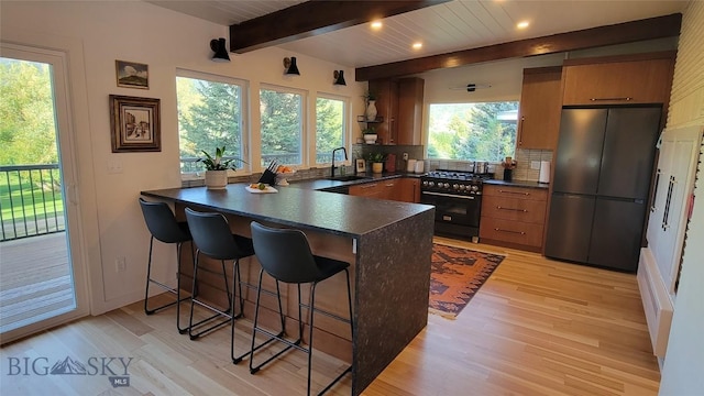 kitchen with dark countertops, high end range, a sink, freestanding refrigerator, and a peninsula