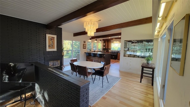 dining area featuring a brick fireplace, light wood-type flooring, beam ceiling, and a chandelier