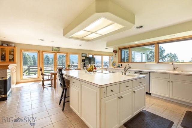 kitchen featuring a center island with sink, dishwasher, a sink, white cabinets, and light tile patterned flooring