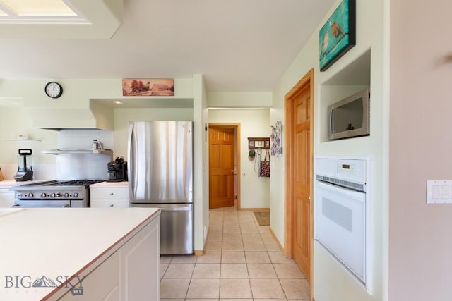 kitchen featuring light tile patterned flooring, light countertops, white cabinets, tasteful backsplash, and appliances with stainless steel finishes