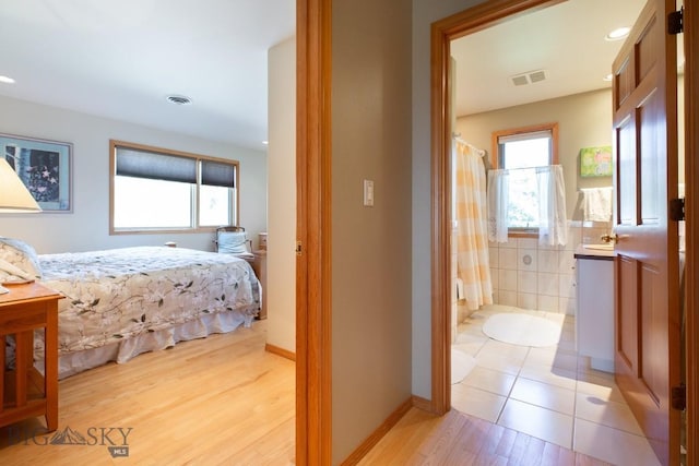 bedroom with visible vents, light wood finished floors, and ensuite bath