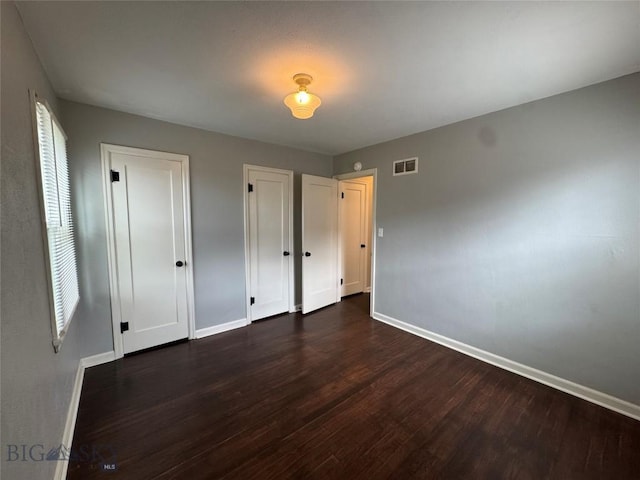 216 W 2nd Ave, Big Timber, MT 59011 - unfurnished bedroom with baseboards, dark wood-style flooring, multiple closets, and visible vents