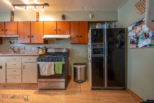 124 S M St, Livingston, MT 59047 - kitchen with black fridge, a sink, light wood-style floors, stainless steel range with gas cooktop, and under cabinet range hood