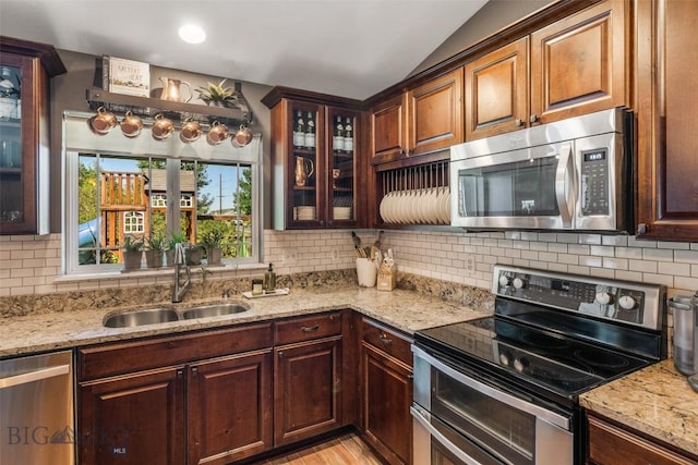 kitchen featuring appliances with stainless steel finishes, a sink, vaulted ceiling, and light stone counters