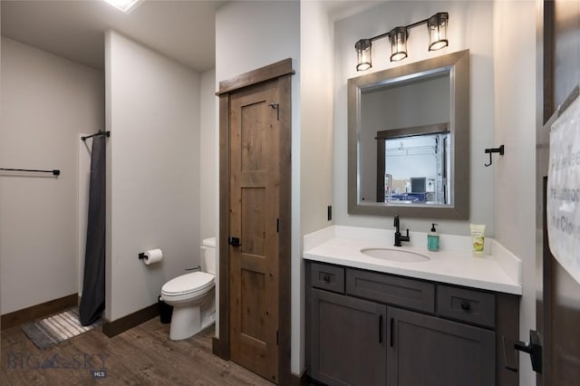 bathroom featuring toilet, baseboards, wood finished floors, and vanity