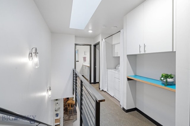hall featuring light colored carpet, baseboards, washer and dryer, and a skylight