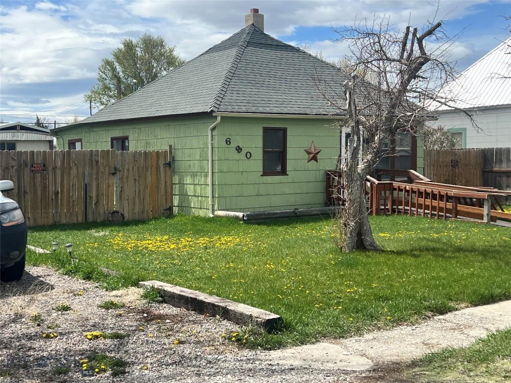 view of property exterior with a yard, fence, a chimney, and roof with shingles