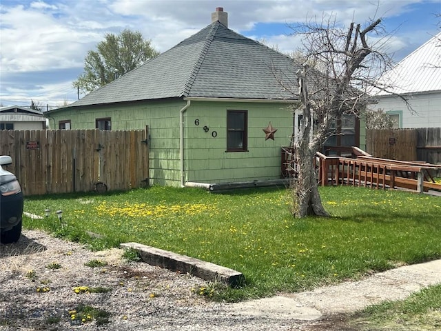 view of property exterior with a yard, fence, a chimney, and roof with shingles