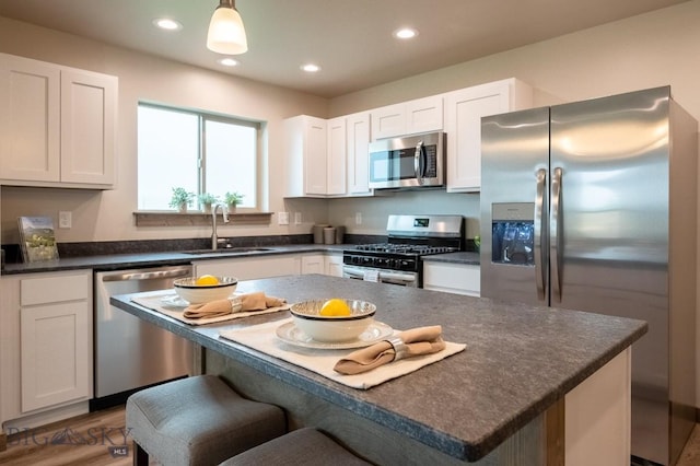 kitchen featuring appliances with stainless steel finishes, dark countertops, a sink, a breakfast bar, and recessed lighting