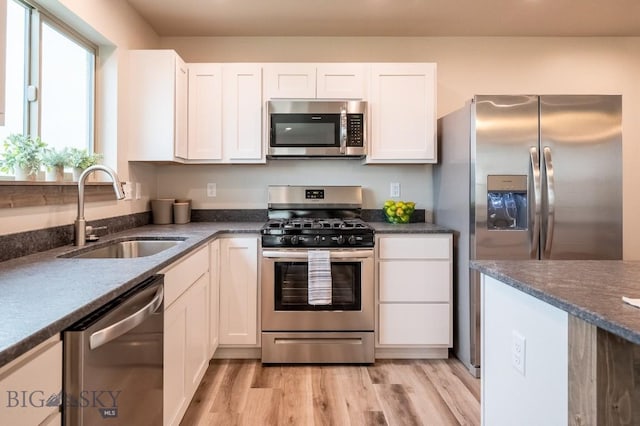 kitchen with a sink, appliances with stainless steel finishes, light wood finished floors, and white cabinetry