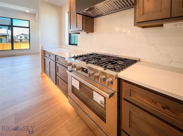kitchen with stainless steel range with gas stovetop, light countertops, light wood-style flooring, premium range hood, and backsplash