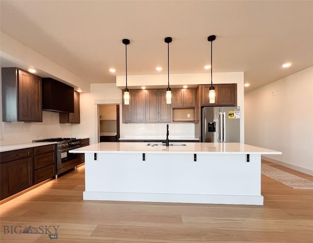 kitchen with a sink, light countertops, an island with sink, light wood-style flooring, and stainless steel appliances