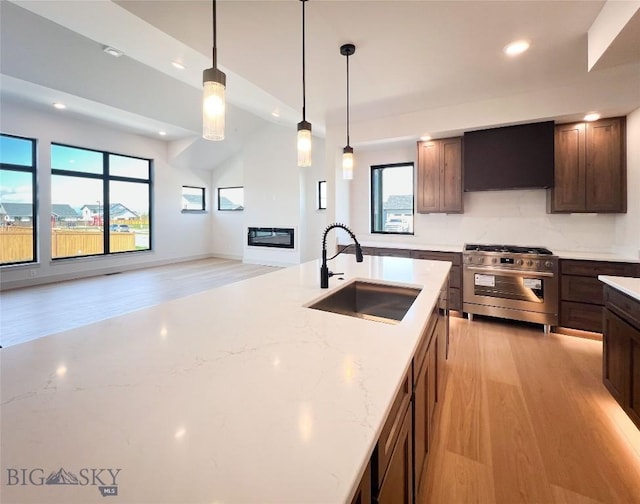kitchen featuring stainless steel range with gas cooktop, a sink, light wood-style flooring, and ventilation hood