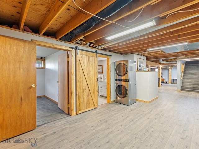 finished basement featuring a barn door, stacked washing maching and dryer, wood finished floors, and stairway