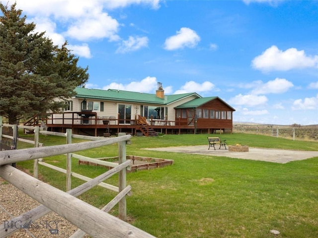 back of property with metal roof, a lawn, a deck, fence, and an outdoor fire pit