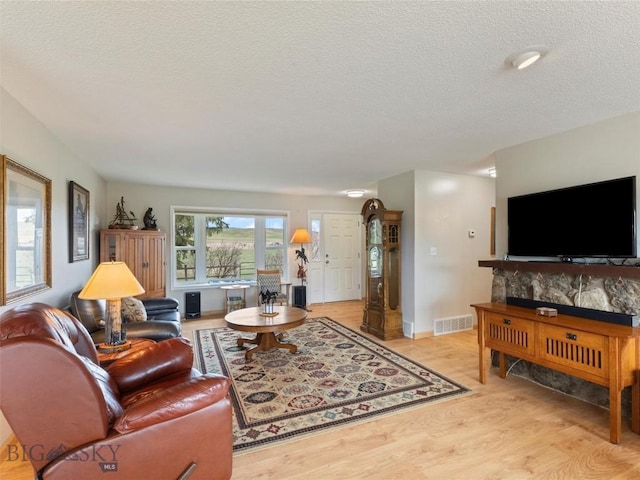 living area featuring light wood-type flooring, a textured ceiling, baseboards, and visible vents