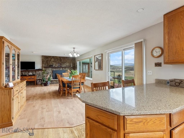 kitchen featuring an inviting chandelier, light stone countertops, a peninsula, open floor plan, and light wood-style floors