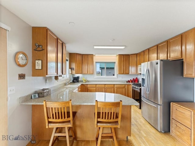kitchen featuring stainless steel refrigerator with ice dispenser, gas range, a sink, a peninsula, and light wood-style flooring