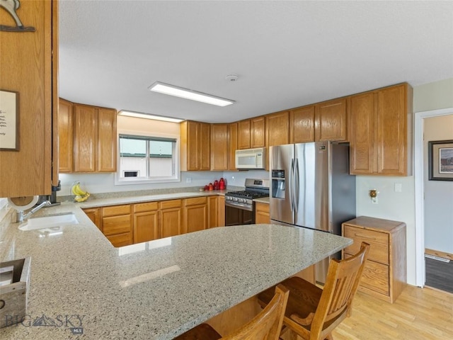 kitchen featuring light stone counters, light wood-style flooring, stainless steel appliances, a peninsula, and a kitchen bar