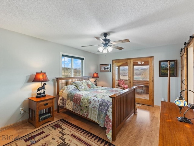 bedroom featuring access to outside, a barn door, light wood-style flooring, and a textured ceiling