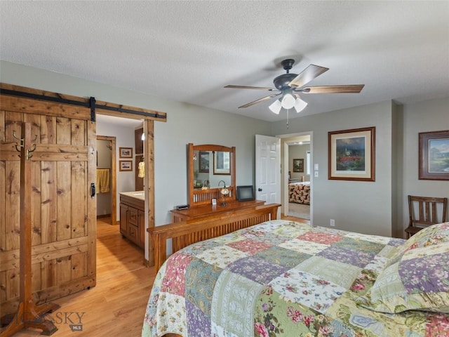 bedroom featuring a barn door, light wood finished floors, a ceiling fan, and a textured ceiling