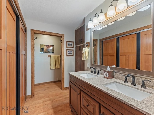 bathroom featuring double vanity, a sink, a textured ceiling, and wood finished floors