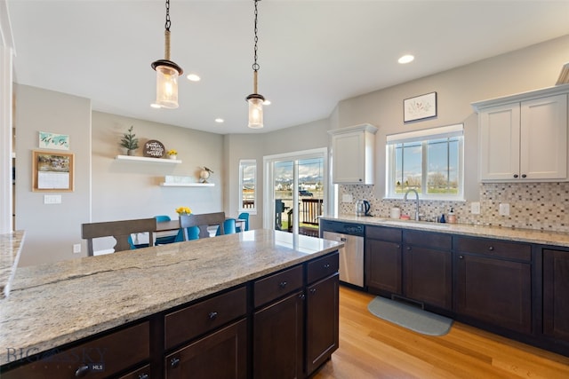 kitchen with stainless steel dishwasher, a sink, light wood finished floors, and decorative backsplash
