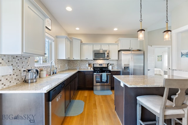 kitchen featuring a breakfast bar, white cabinetry, a sink, light wood-style flooring, and stainless steel appliances