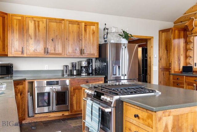 kitchen with brown cabinets, stone finish flooring, dark countertops, and appliances with stainless steel finishes
