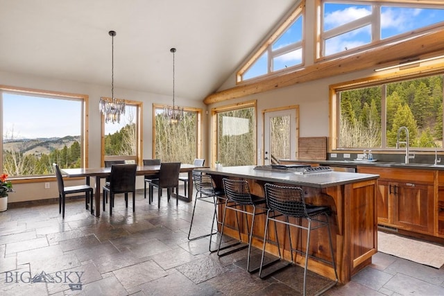 kitchen featuring brown cabinets, a notable chandelier, a sink, stainless steel gas stovetop, and stone tile flooring